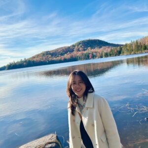 Siyu poses in front of a large body of water and fall foliage